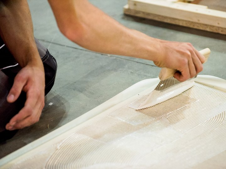 Bodenleger Person trägt Fliesenkleber mit Zahnspachtel auf Boden auf