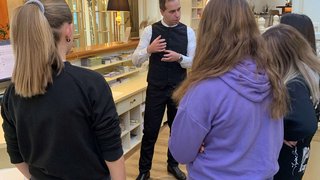 Junghandwerker Hotelmitarbeiter erklärt einer Gruppe junger Gäste die Abläufe an der Rezeption