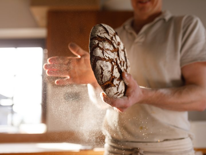 Bäcker Person hält frisch gebackenes Brot mit Mehlstaub in der Luft