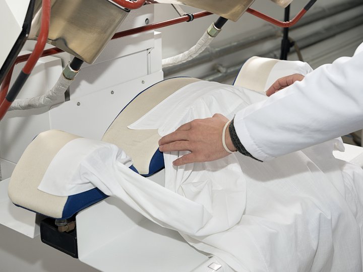 Textilreiniger Person legt weißes Hemd auf Bügelmaschine zum Bügeln