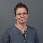 Floristen Porträt einer lächelnden Frau mit Brille und kurzem Haar vor grauem Hintergrund