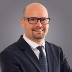 Das lvh-Team Lächelnder Mann mit Brille im Anzug vor grauem Hintergrund