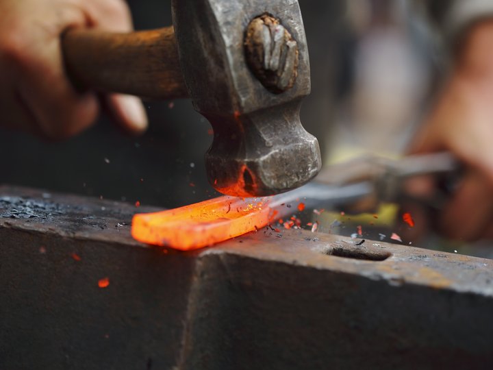 Schmiede und Schlosser Schmied arbeitet mit Hammer auf glühendem Metallstück auf Amboss
