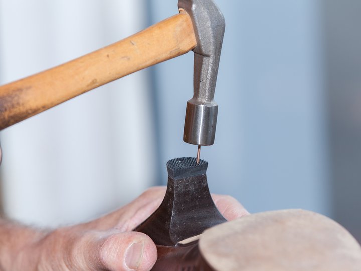 Schuhmacher Hand hält Hammerschuhsohle, Nagel wird mit Hammer eingeschlagen