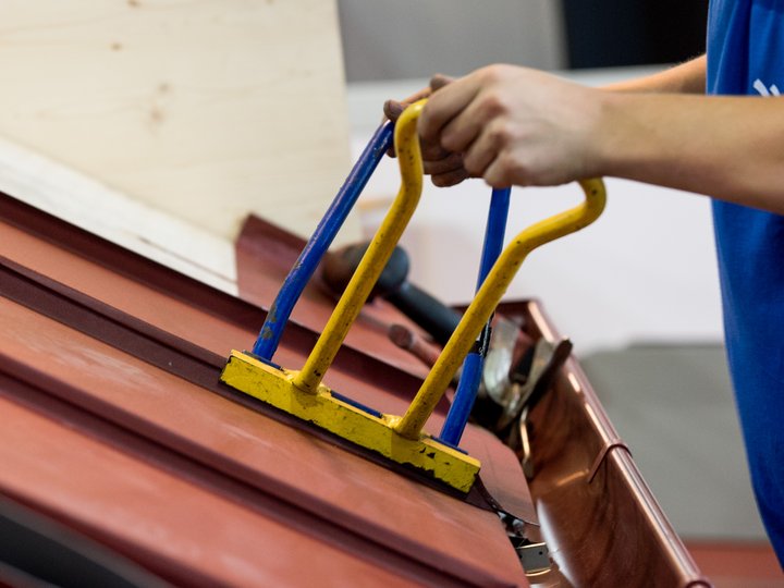 Bau- und Galanteriespengler Person befestigt Metallblech am Dach mit Werkzeug