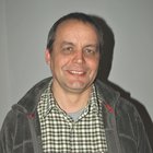 Holzbaumeister und Zimmerer Mann mittleren Alters in kariertem Hemd und grauer Jacke lächelnd vor weißer Wand