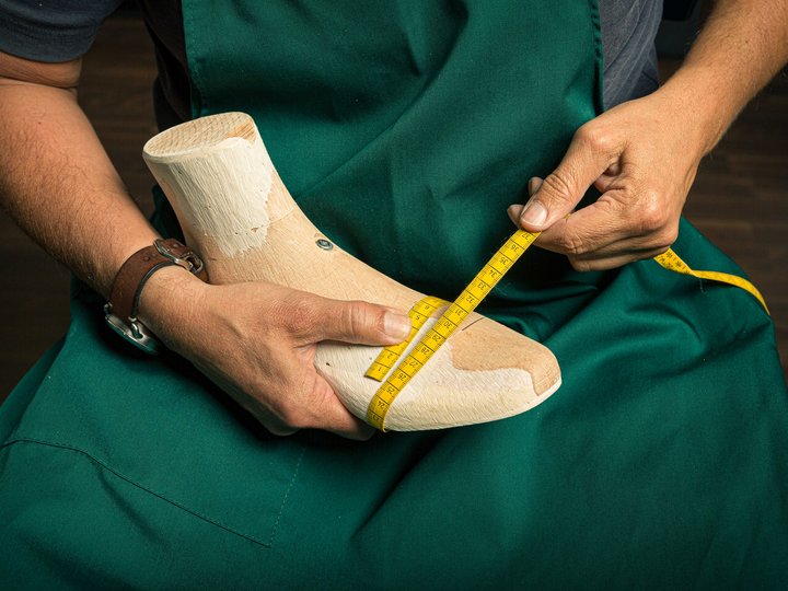 Orthopädieschuhmacher Schuhmacher misst Holzleisten mit Maßband in grüner Schürze