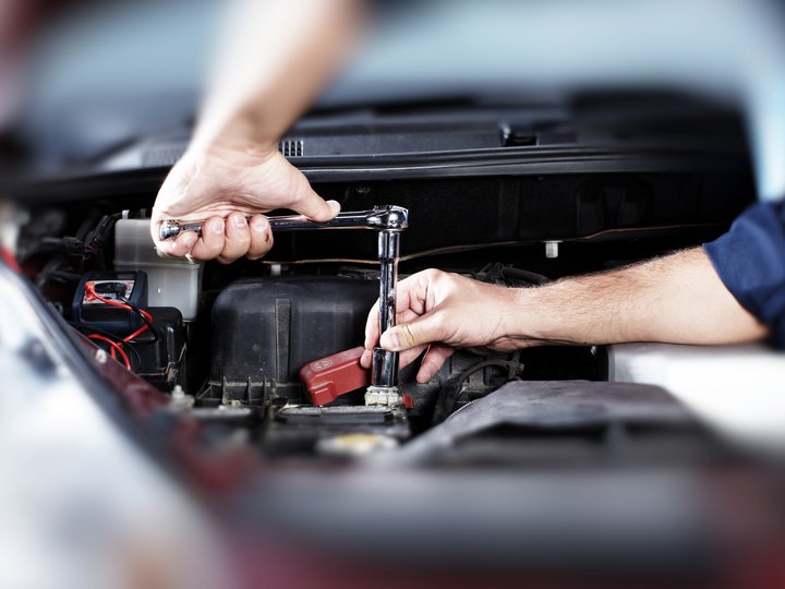 Kfz-Mechatroniker Mechaniker zieht Schraube im Motorraum eines Autos mit Ratsche fest