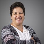 Das lvh-Team Lächelnde Frau mit kurzen Haaren und gemusterter Jacke vor grauem Hintergrund