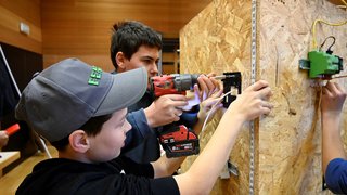 Junghandwerker Zwei Jugendliche montieren eine elektrische Installation auf einer Holzplatte