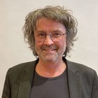 Maler und Lackierer Mann mit Brille, grauen lockigen Haaren und Bart lächelt freundlich