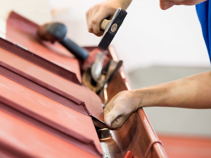 Bau- und Galanteriespengler Handwerker repariert rotes Dach mit Hammer