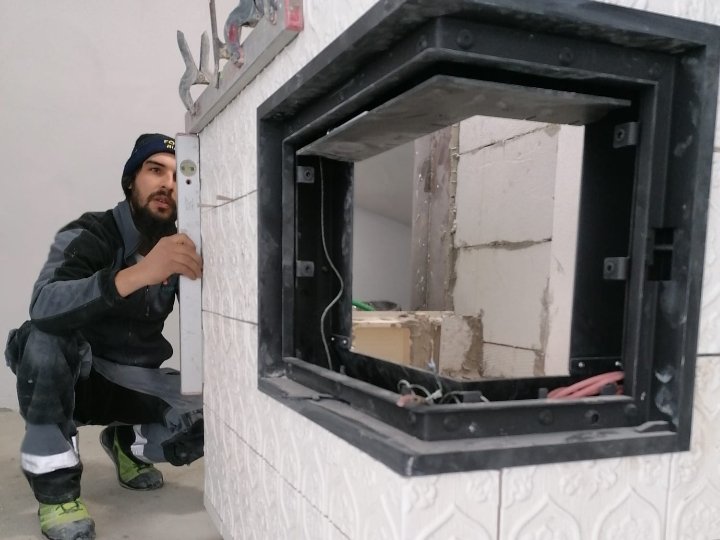 Hafner Handwerker installiert Kamin mit weißen Kacheln und schwarzem Metallrahmen