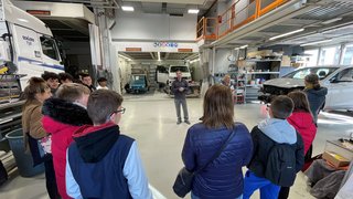 Junghandwerker Gruppe von Menschen hört in Werkstatt einem Mann bei einer Präsentation zu