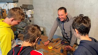 Junghandwerker Erwachsener erklärt Jugendlichen Werkzeuge auf Werkbank in Werkstatt