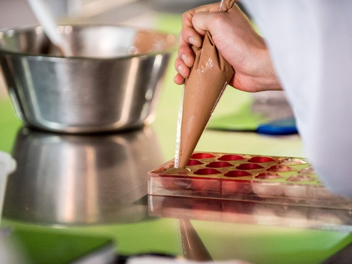 Konditoren Hand füllt Schokoladenform mit Schokoladencreme aus Spritztüte