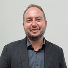 Tiefbauunternehmer Portrait eines lächelnden Mannes mit kurzem Bart und Anzugjacke vor heller Wand