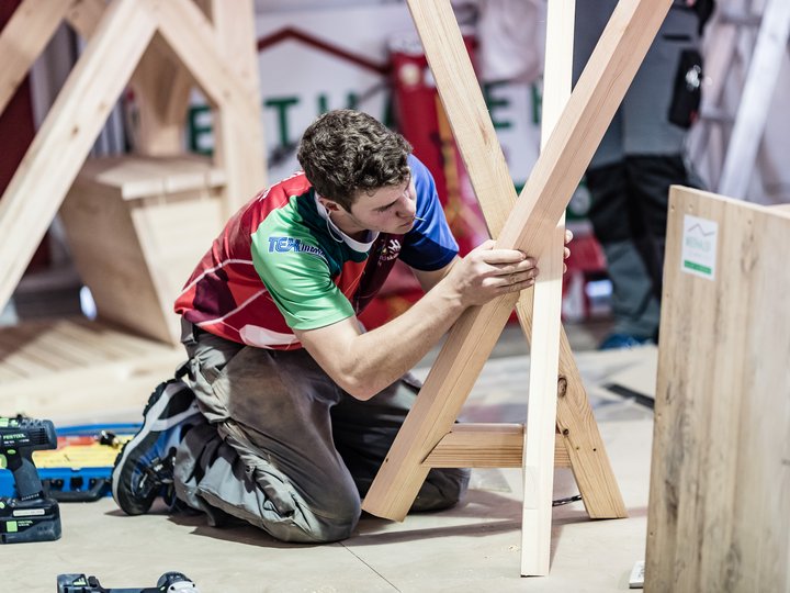 Holzbaumeister und Zimmerer Mann kniet und arbeitet an Holzkonstruktion mit Werkzeug auf Boden