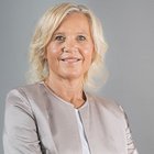 Frauen im Handwerk Porträt einer lächelnden älteren Frau mit heller Jacke vor grauem Hintergrund