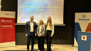 Frauen im Handwerk Drei Personen stehen vor einer Leinwand mit Vortrag zu Geldanlage und Bankenbanner