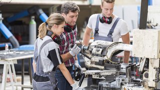 Berufsbildung Drei Mechaniker arbeiten zusammen an einer Metallbandsäge in der Werkstatt