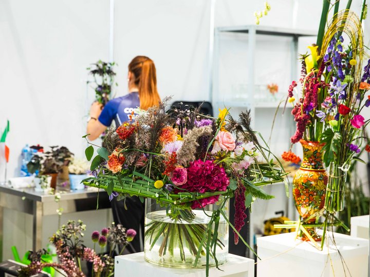 Floristen Bunte Blumenarrangements in Glasvasen auf Podesten vor einer Frau mit Pferdeschwanz