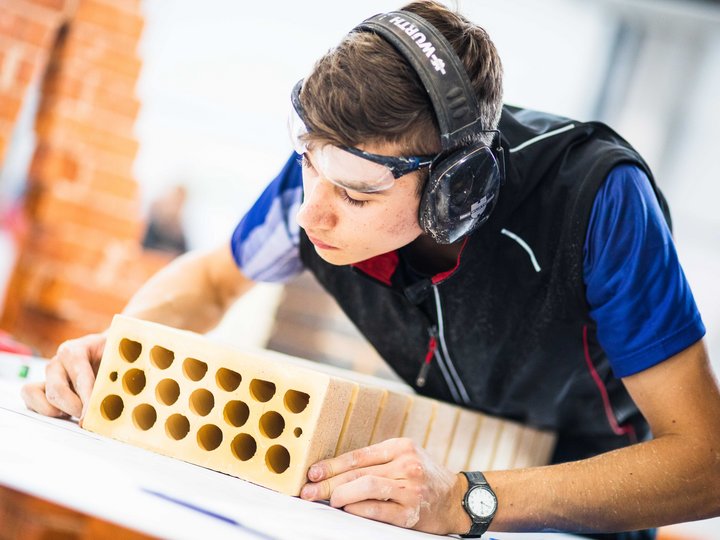 Baumeister und Maurer Junger Mann begutachtet Ziegelstein mit Schutzbrille und Gehörschutz