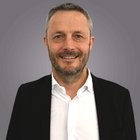 Steuerberatung, Buchhaltung und Lohnabrechnung Porträt eines lächelnden Mannes mit Bart in schwarzem Sakko und weißem Hemd vor grauem Hintergrund