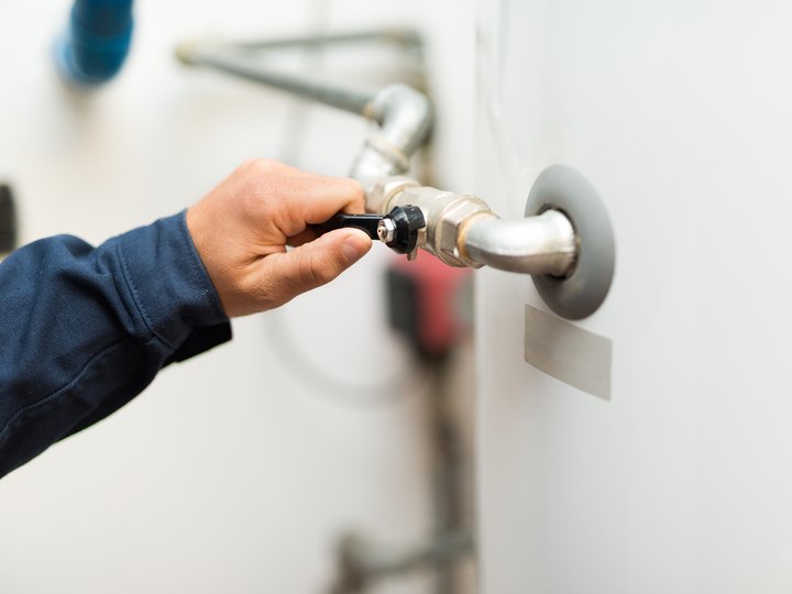 Feuerungstechniker Hand bedient ein Ventil an Rohrleitung an einer weißen Wand