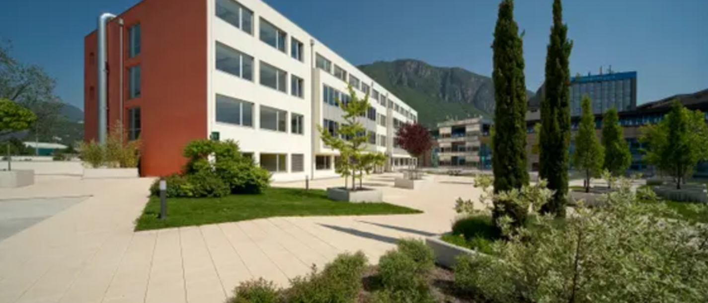 Berufsbildung Moderne Gebäude mit Terrasse und Bäumen vor Bergkulisse bei klarem Himmel