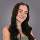 Gründung und Nachfolge Junge Frau mit langen, dunklen Haaren und grünem Oberteil lächelt vor grauem Hintergrund