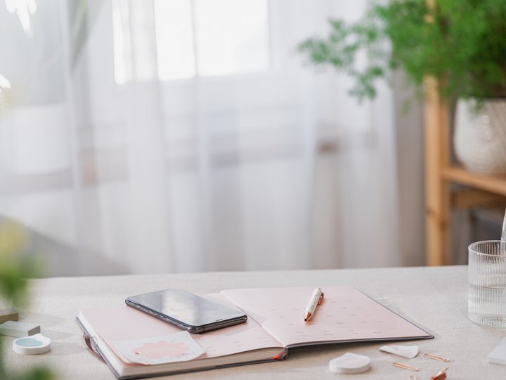 Nachhaltiges Handwerk Smartphone auf offenem Planer auf Tisch neben Glas Wasser und Pflanzen