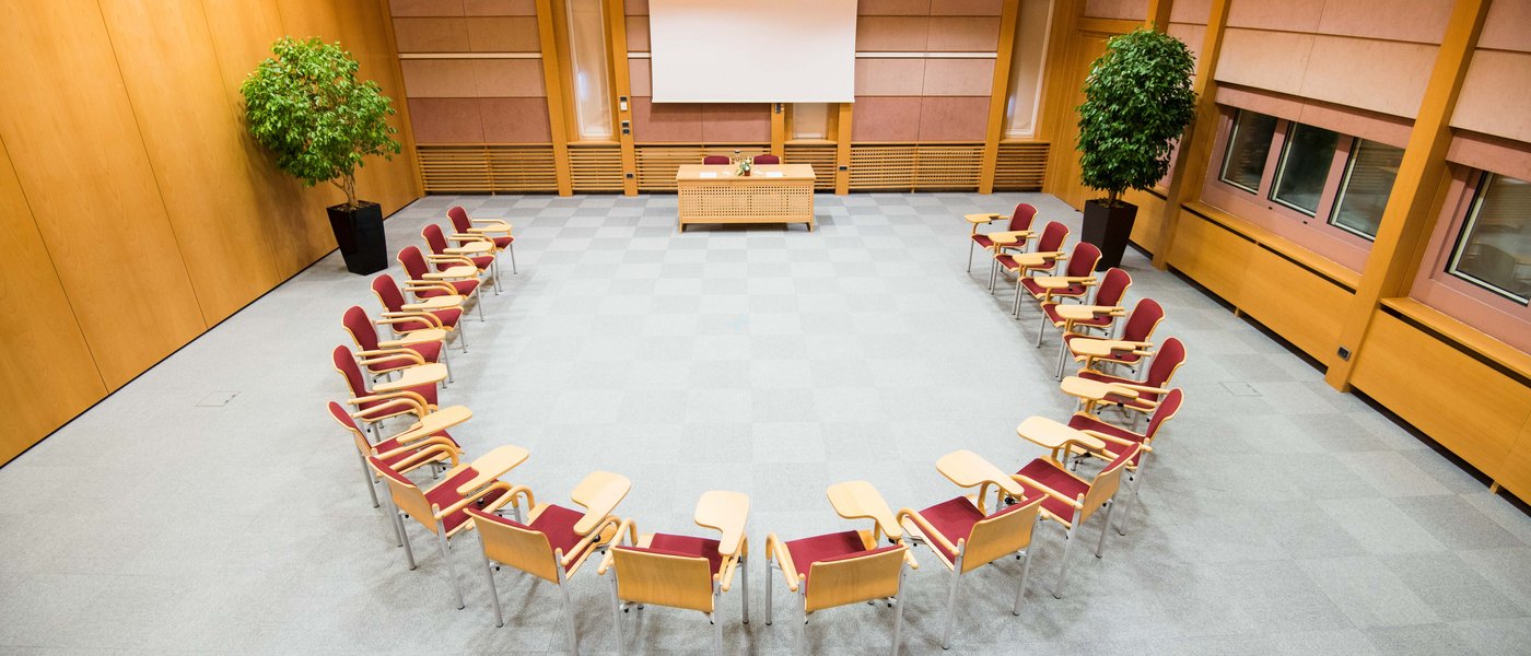 Vermietung Seminarräume Konferenzraum mit Stühlen im Halbkreis vor einem Tisch und einer Leinwand