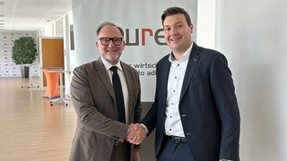 Junghandwerker Zwei Männer im Anzug geben sich in einem Büro die Hand