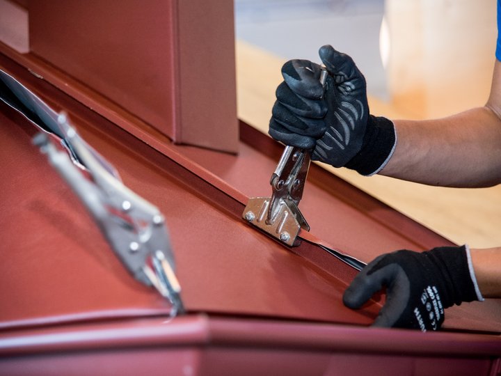 Bau- und Galanteriespengler Handwerker repariert rotes Metalldach mit Zange und Schraube
