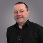 Öffentliche Förderungen und Nuova Sabatini Porträt eines lächelnden Mannes mit schwarzem Hemd vor grauem Hintergrund