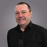 Das lvh-Team Porträt eines lächelnden Mannes mit schwarzem Hemd vor grauem Hintergrund