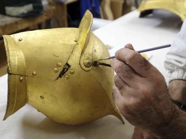 Restauratoren Hand restauriert ein altes goldenes Ritterhelm mit einem Pinsel