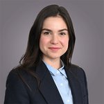 Das lvh-Team Porträt einer lächelnden jungen Frau mit blauer Bluse und dunklem Blazer vor grauem Hintergrund