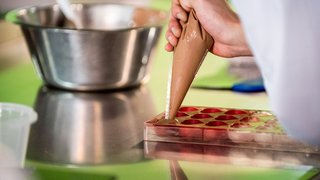 News Hand füllt Pralinenform mit flüssiger Schokolade