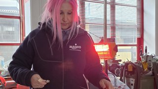 Frauen im Handwerk Frau mit pinken Haaren in Werkstatt hält kleine Teile in der Hand