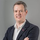 Nachhaltiges Handwerk Porträt eines lächelnden Mannes mit verschränkten Armen vor grauem Hintergrund