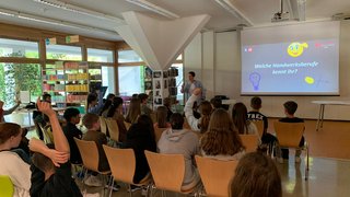 Junghandwerker Schüler heben Hände in Vortrag über Handwerksberufe im Klassenzimmer