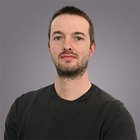 Steuerberatung, Buchhaltung und Lohnabrechnung Porträt eines jungen Mannes mit kurzem Haar und Bart vor grauem Hintergrund