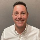 Feuerungstechniker Lächelnder Mann mit kurzem Haar und weißem Hemd vor grauer Wand