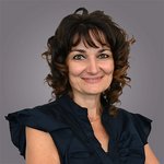 Das lvh-Team Porträt einer lächelnden Frau mit lockigem Haar vor grauem Hintergrund