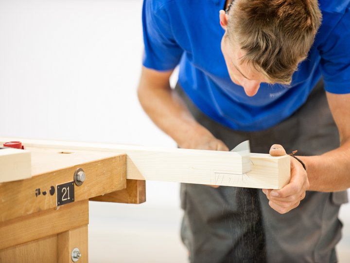 Holzbaumeister und Zimmerer Mann bearbeitet ein Holzstück mit Handhobel an Werkbank