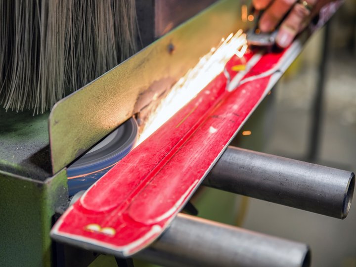 Sportgerätetechniker Schleifen einer roten Skikante mit Funken