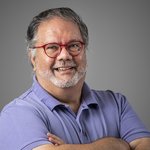 Das lvh-Team Lächelnder Mann mit roter Brille und violettem Polohemd vor grauem Hintergrund