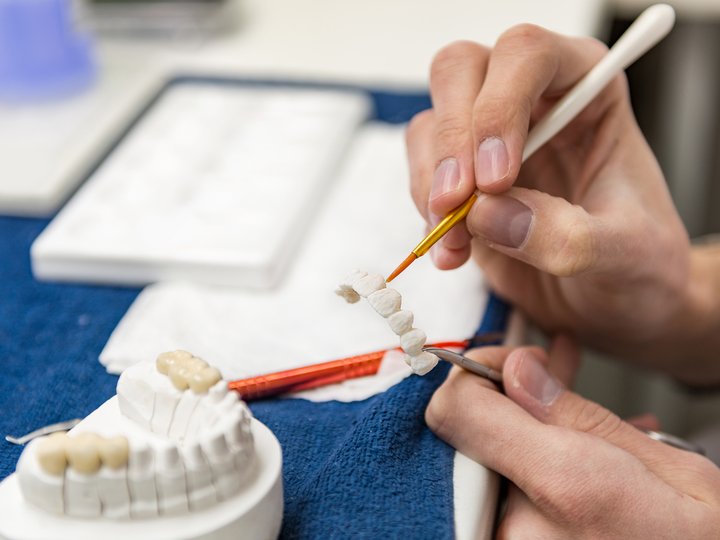 Zahntechniker Zahntechniker bemalt Zahnbrücke mit feinem Pinsel im Labor